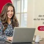 Mujer sonriente usando una laptop en una mesa, con un fondo claro y el logo de FEMSA. La imagen destaca la importancia del talento humano en la empresa, invitando a conocer más sobre la organización.