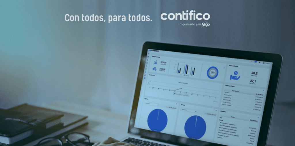 Pantalla de computadora portátil mostrando un dashboard de análisis de datos de Contifico, con gráficos y métricas financieras, acompañado de un cuaderno y gafas en la mesa.