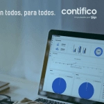 Pantalla de computadora portátil mostrando un dashboard de análisis de datos de Contifico, con gráficos y métricas financieras, acompañado de un cuaderno y gafas en la mesa.