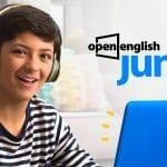 Niño sonriente usando auriculares mientras estudia en una computadora portátil azul, promoviendo el programa Open English Junior.